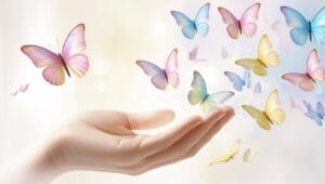Main ouverte laissant s’envoler des papillons lumineux, symbolisant la libération émotionnelle et la transformation.
