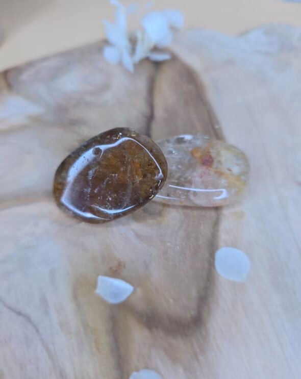 Deux pierres roulées de citrine sur une surface en bois clair avec quelques pétales blancs éparpillés autour.