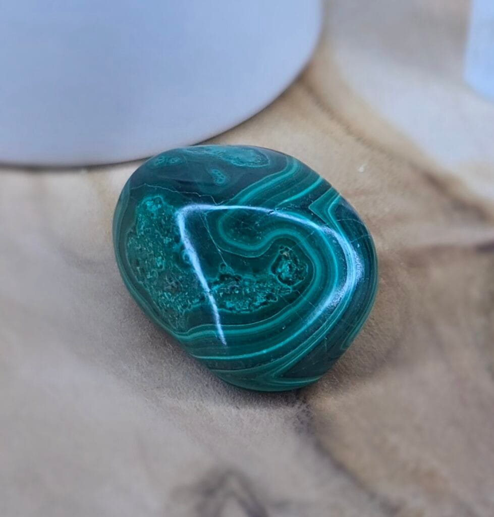 Pierre roulée de malachite verte posée sur une surface en bois naturel, montrant ses motifs concentriques uniques.