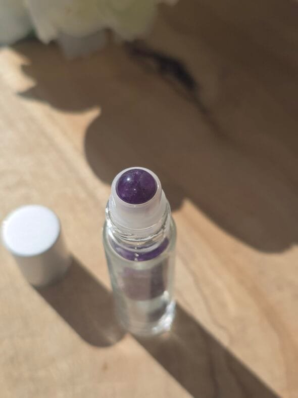 Roll-on en améthyste poli rempli d’huile essentielle, posé sur une surface naturelle