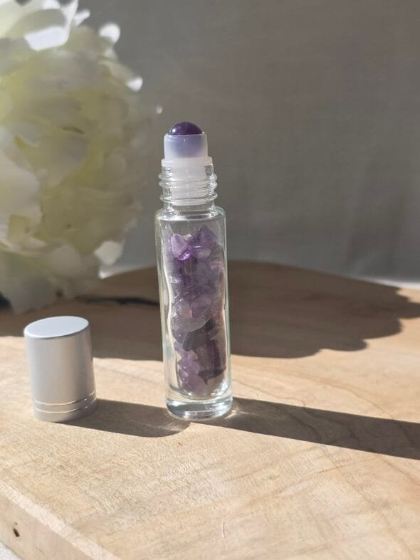 Roll-on en améthyste poli rempli d’huile essentielle, posé sur une surface naturelle