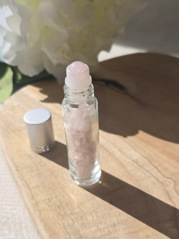 Roll-on en quartz rose poli rempli d’huile essentielle, posé sur du bois