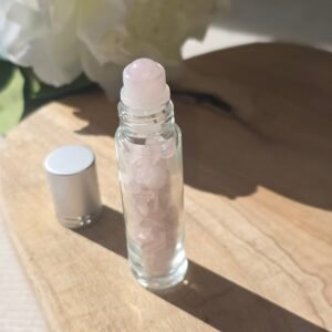 Roll-on en quartz rose poli rempli d’huile essentielle, posé sur du bois