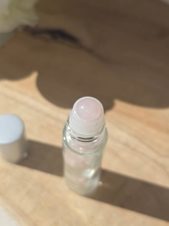 Roll-on en quartz rose poli rempli d’huile essentielle, posé sur du bois