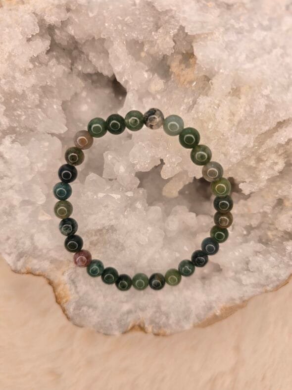 Bracelet en agate indienne naturelle de 6 mm, posé sur une géode de quartz blanc.