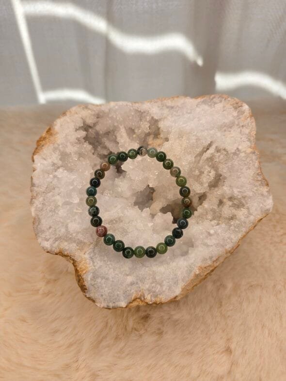 Bracelet en agate indienne naturelle de 6 mm, posé sur une géode de quartz blanc.