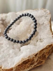 Bracelet en perles naturelles d’hématite noire brillante, diamètre 6 mm, posé sur une géode de quartz
