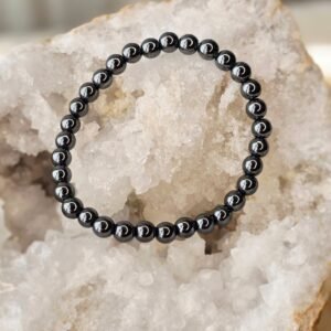 Bracelet en perles naturelles d’hématite noire brillante, diamètre 6 mm, posé sur une géode de quartz