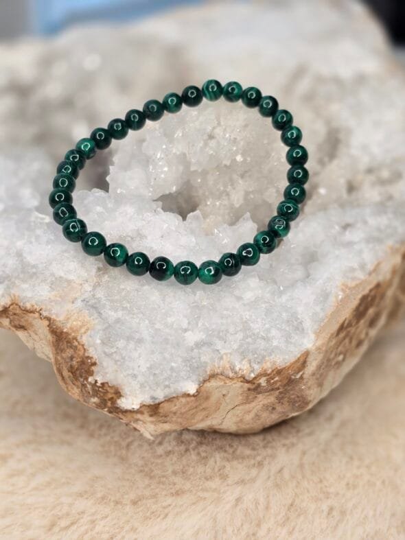 Bracelet en perles naturelles de malachite foncée 6 mm posé délicatement sur une géode de quartz