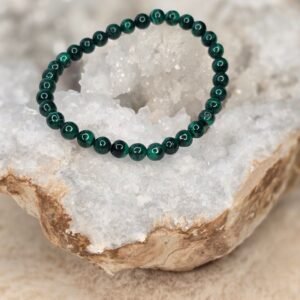 Bracelet en perles naturelles de malachite foncée 6 mm posé délicatement sur une géode de quartz