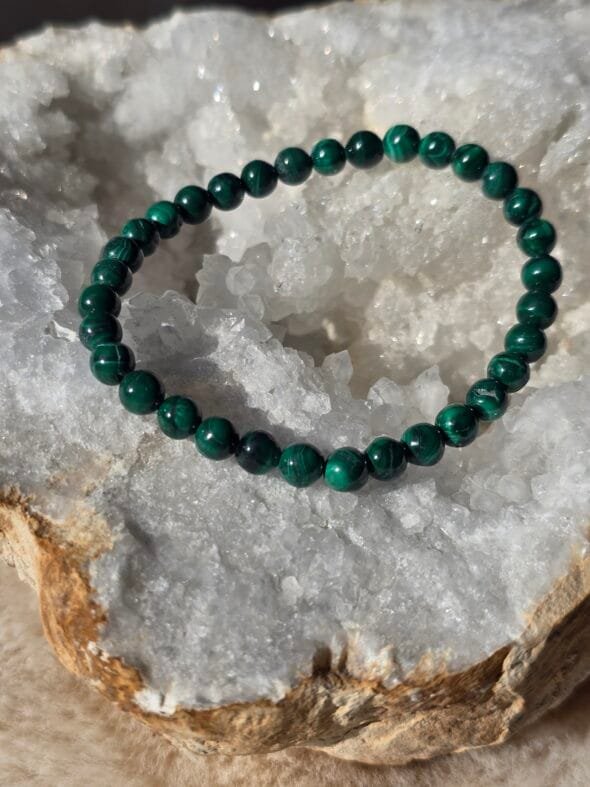 Bracelet en perles naturelles de malachite foncée 6 mm posé délicatement sur une géode de quartz