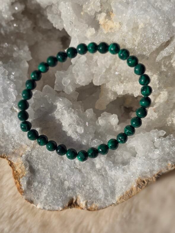 Bracelet en perles naturelles de malachite foncée 6 mm posé délicatement sur une géode de quartz