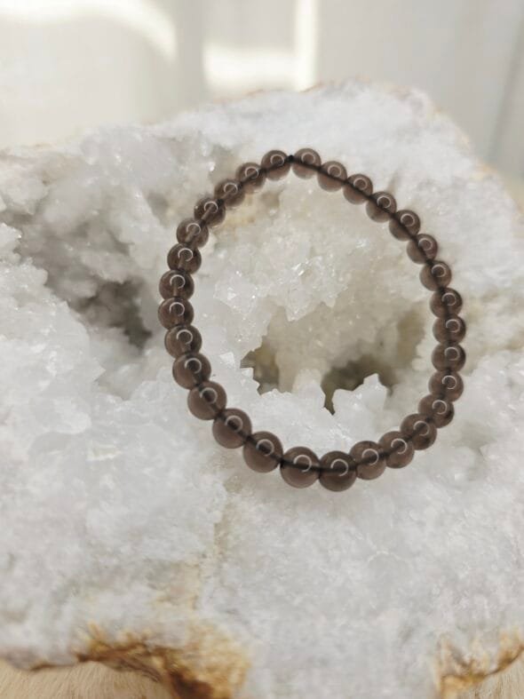 Bracelet en perles naturelles d’obsidienne Larme d’Apache 6 mm posé sur géode quartz