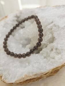 Bracelet en perles naturelles d’obsidienne Larme d’Apache 6 mm posé sur géode quartz