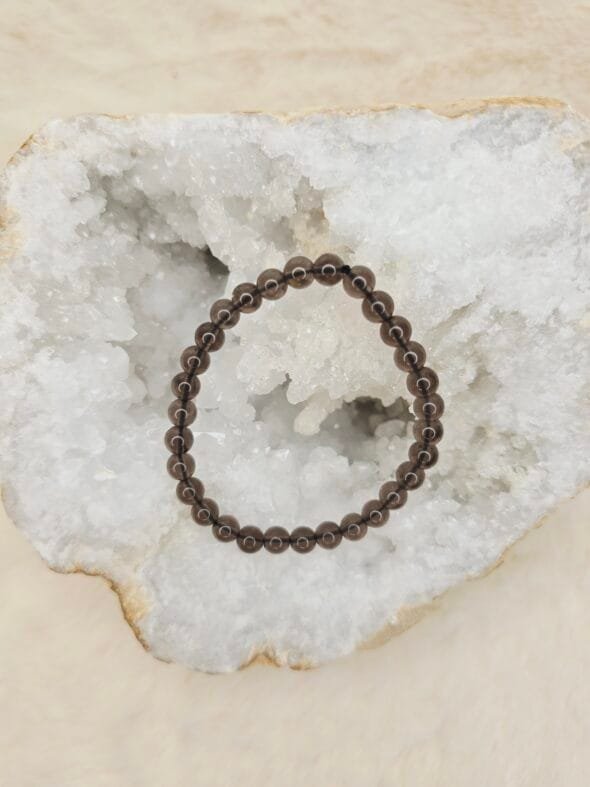 Bracelet en perles naturelles d’obsidienne Larme d’Apache 6 mm posé sur géode quartz