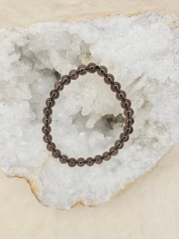 Bracelet en perles naturelles d’obsidienne Larme d’Apache 6 mm posé sur géode quartz