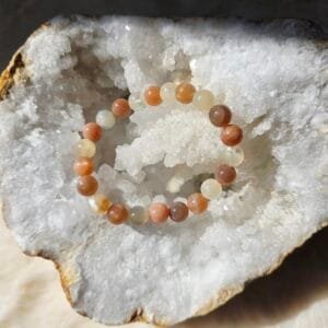 Bracelet en perles naturelles de pierre de lune 8 mm posé sur une géode de quartz blanc.