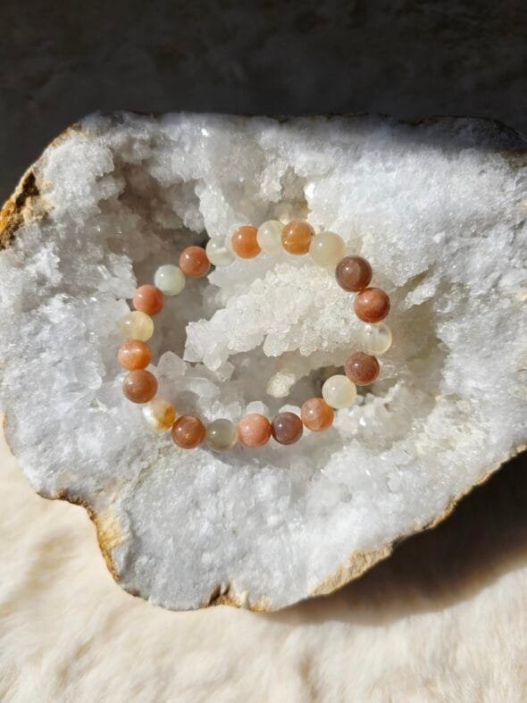 Bracelet en perles naturelles de pierre de lune 8 mm posé sur une géode de quartz blanc.