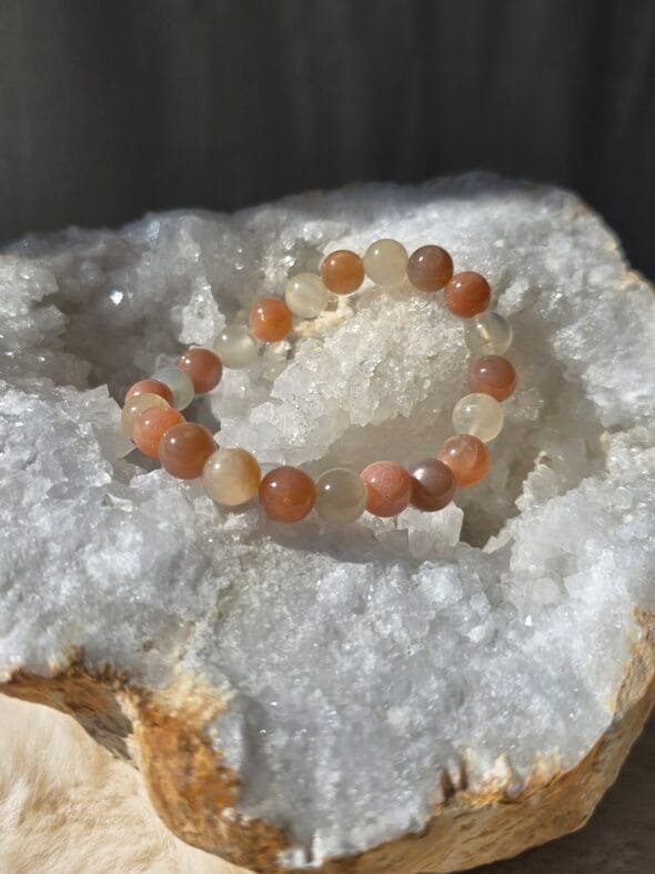 Bracelet en perles naturelles de pierre de lune 8 mm posé sur une géode de quartz blanc.