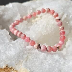Bracelet en perles naturelles de Rhodochrosite 6 mm posé sur une géode de quartz