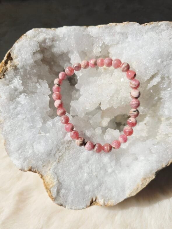 Bracelet en perles naturelles de Rhodochrosite 6 mm posé sur une géode de quartz