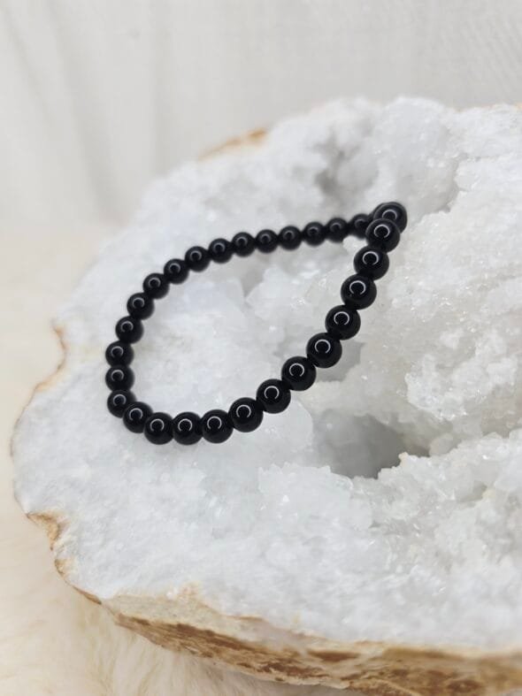 Pierre brute de tourmaline noire posée sur une géode de quartz blanc cristallin.
