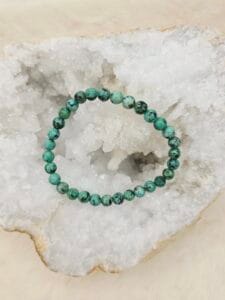 Bracelet en turquoise d’Afrique 8 mm, pierre naturelle aux nuances vertes et brunes, posé sur une géode.