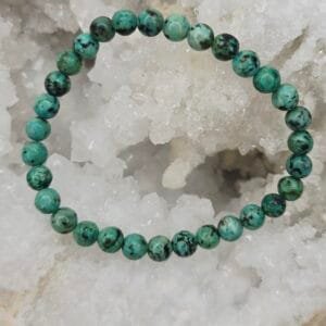 Bracelet en turquoise d’Afrique 8 mm, pierre naturelle aux nuances vertes et brunes, posé sur une géode.