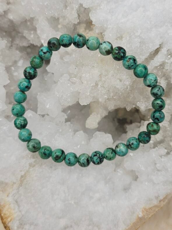 Bracelet en turquoise d’Afrique 8 mm, pierre naturelle aux nuances vertes et brunes, posé sur une géode.