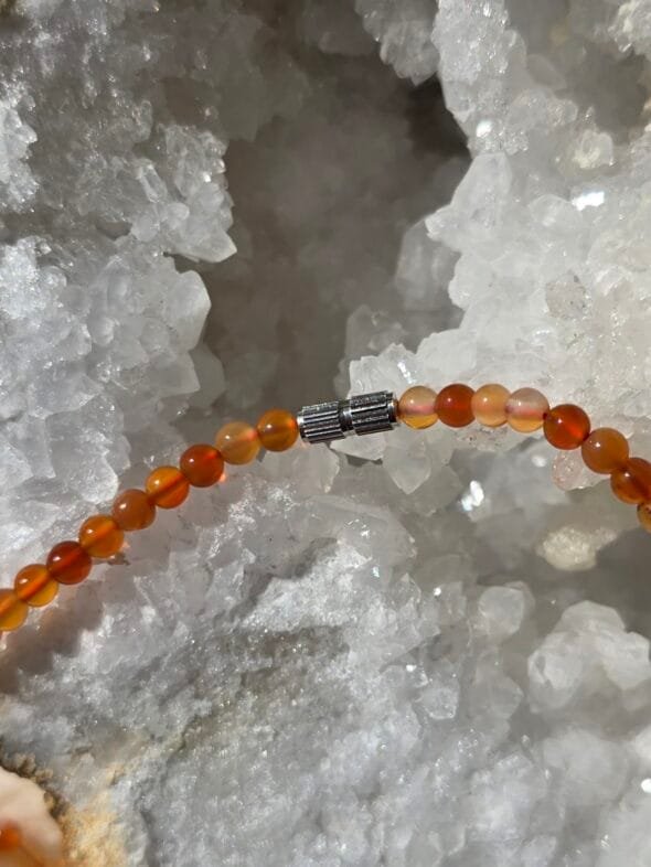 Collier en perles naturelles de cornaline 4 mm posé sur une géode, bijou artisanal et énergétique.