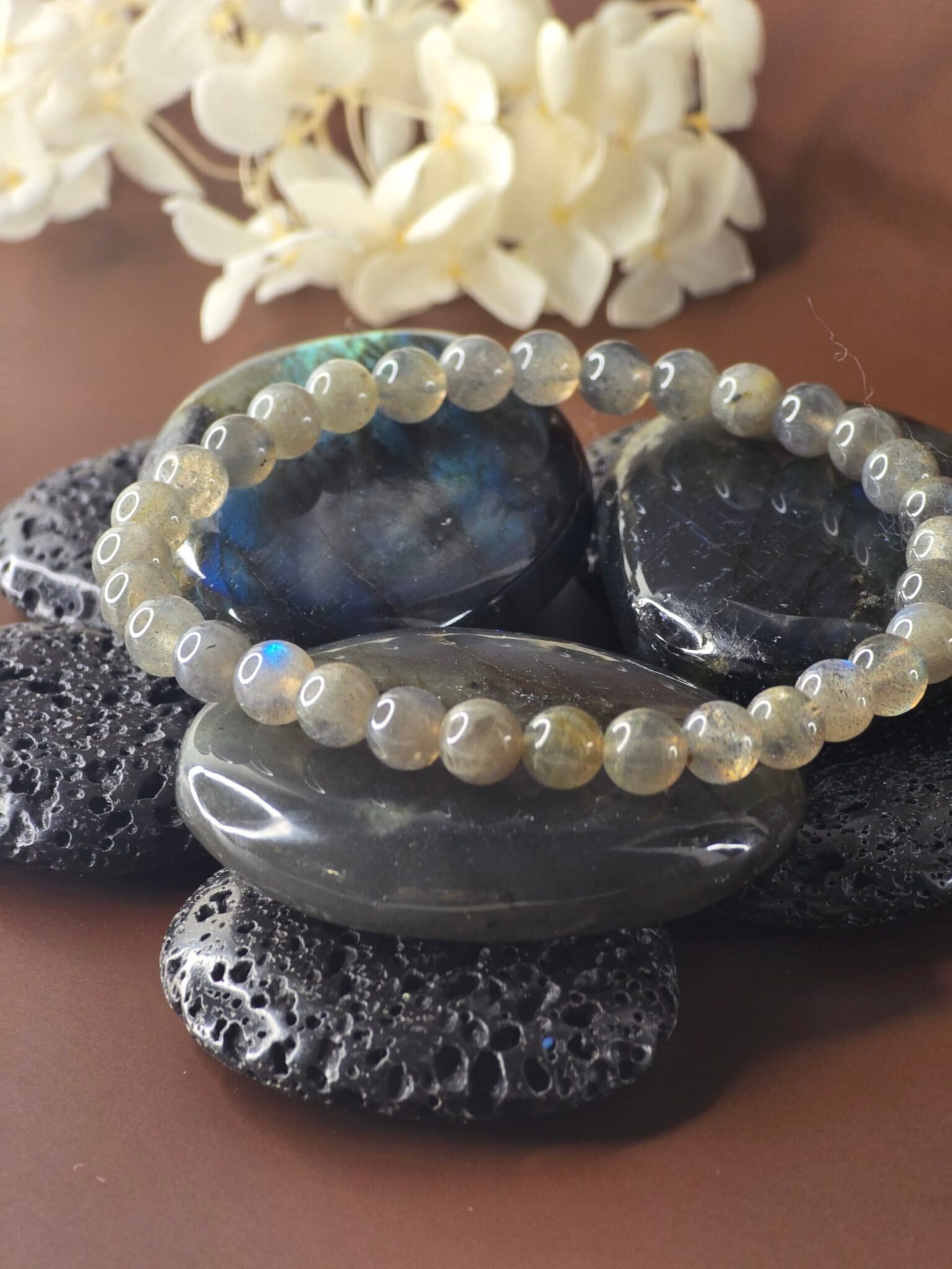 Bracelet en labradorite posé sur des galets de labradorite et pierres de lave, ambiance naturelle et énergétique